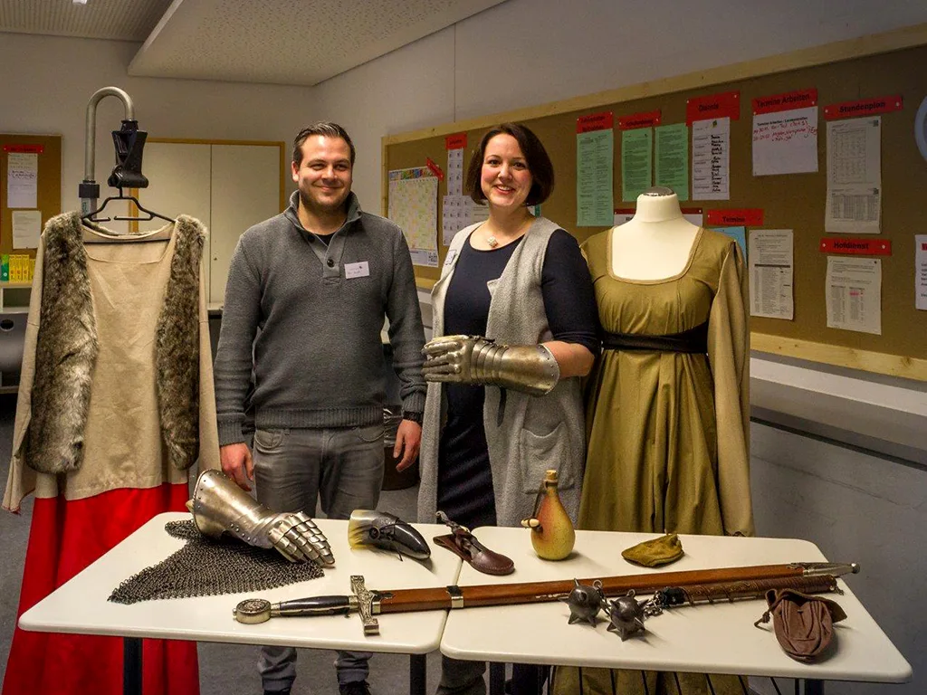 Zwei Erwachsene stehen an einem Tisch mit historischen Waffen und Kleidungsstücken.